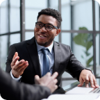A sharply dressed businessman speaks to a colleague in a well-lit office. 